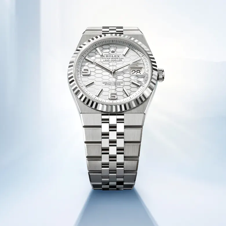 rolex Land-Dweller    - Questo quadrante blu ghiaccio, un colore riservato agli orologi realizzati in platino, è impreziosito dal motivo a nido d’ape con finitura soleil. Per realizzarlo, il Marchio ha fatto ricorso sia alle tecniche tradizionali, sia ai procedimenti di alta tecnologia, tutti perfettamente dominati in‑house. Il taglio degli alveoli e l’esecuzione delle striature all’interno delle scanalature che li separano richiedono l’intervento del laser a femtosecondi. Il quadrante dispone della visualizzazione Chromalight, con numeri aperti e indici luminescenti che gli conferiscono una leggibilità ottimale in ogni circostanza. Le lancette, anch’esse luminescenti, sono state appositamente disegnate per questo modello.